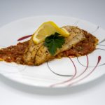 A fish fillet rests on a bed of tomato compote and is topped with parsley and a twist of lemon.