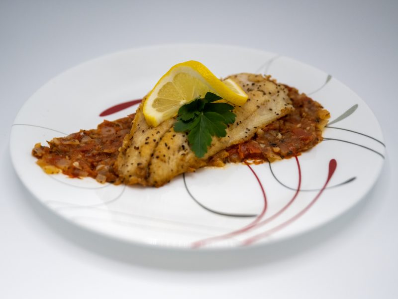 A fish fillet rests on a bed of tomato compote and is topped with parsley and a twist of lemon.