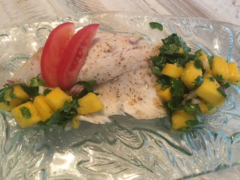 Cooked tilapia with a mango-cilantro salsa and two tomato slices on a glass plate.