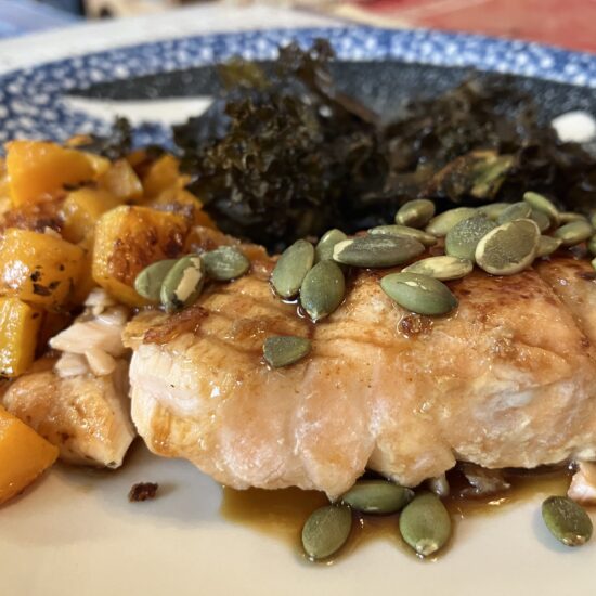Cooked fish sprinkled with pumpkin seeds in front of squash and kale.