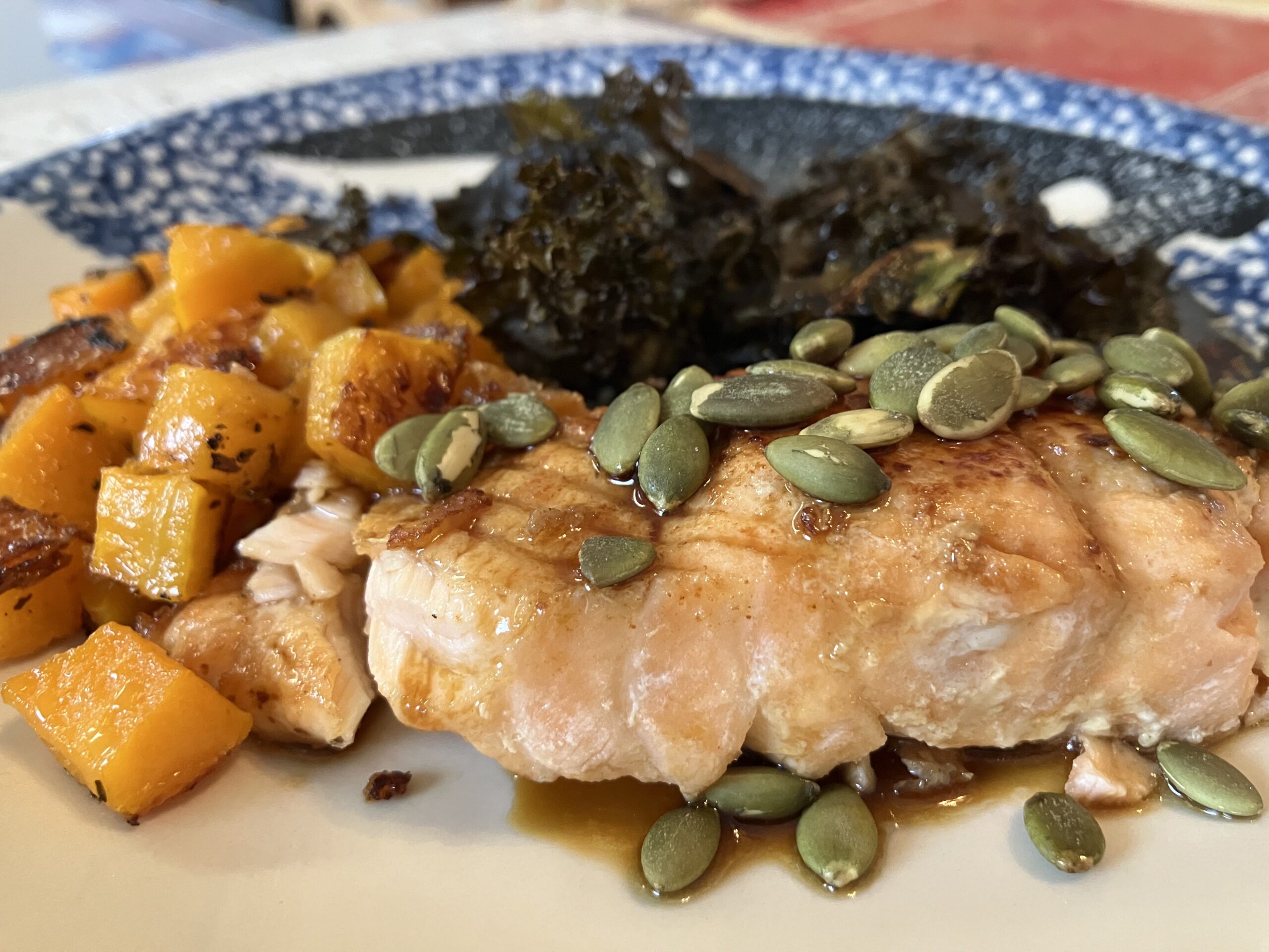Cooked fish sprinkled with pumpkin seeds in front of squash and kale.