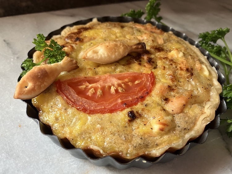 Single fish tart topped with two pastry fish, tomato and parsley.