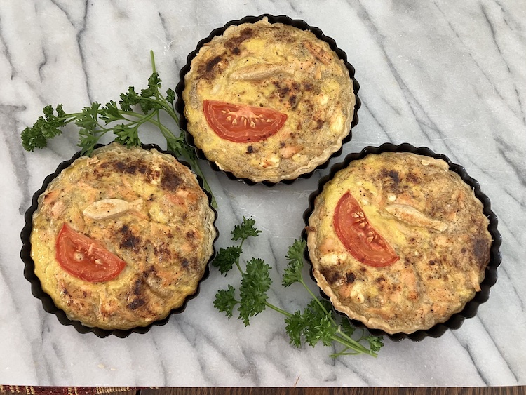 Three fish tarts with parsley on a marble counter.