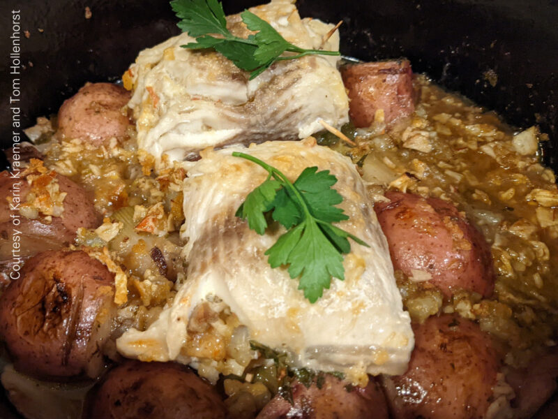 Two stuffed lake whitefish fillets over potatoes and leeks in a cast iron pot.