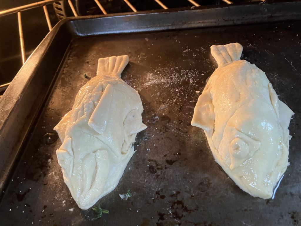 Two fish-shaped pies on a baking tray in an oven.