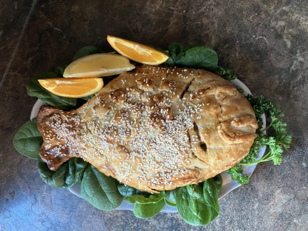 Baked fish-shaped pie displayed with 3 citrus slices and greens.