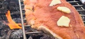 Salmon with butter pats on top on a grate over an open fire.